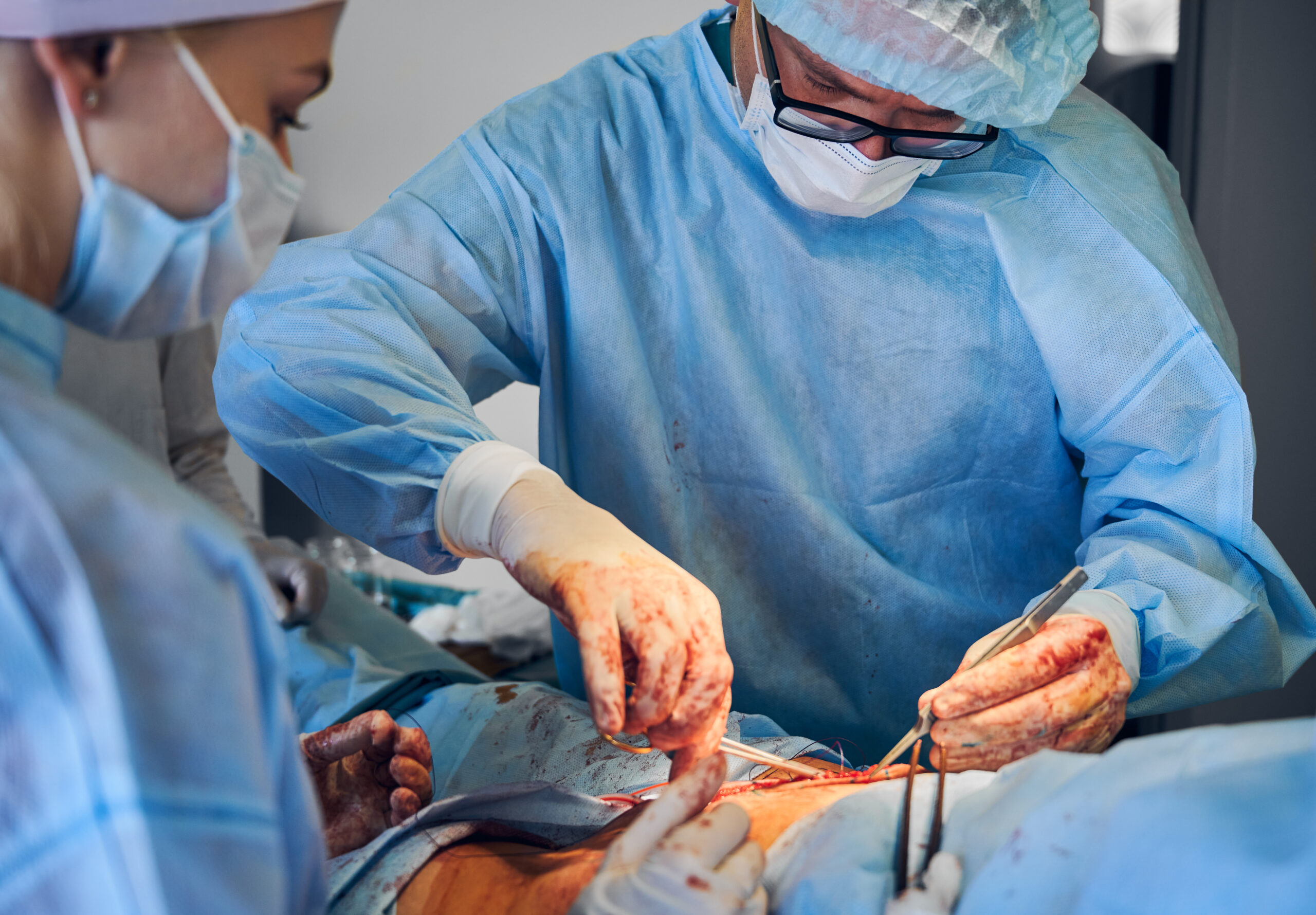 Doctor and assistant doing abdominoplasty surgery in modern clinic.